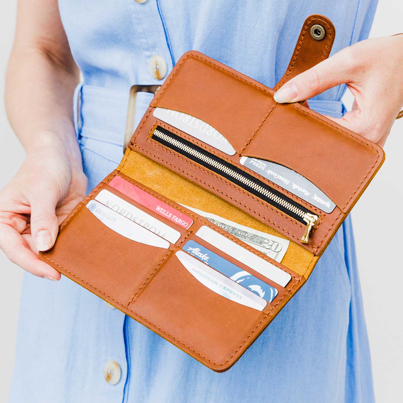 A person holding a brown bifold wallet with cards slots and a zippered pocket, made of leather.