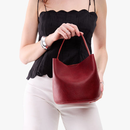 Chili Red*Small | Model holding symmetrical bucket bag with handle, latch closure, and removable crossbody strap