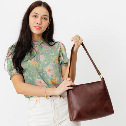 Cognac*Classic | Model holding leather triangular shoulder bag with zipper top closure and wide shoulder strap