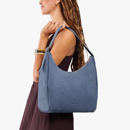 Denim*Large | Model holding u-shaped, flat-bottomed leather shoulder bag with adjustable strap