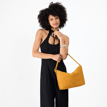 Dijon*Large | Model holding a Slouchy Shoulder Bag that has a zipper opening and three metal tree emblems