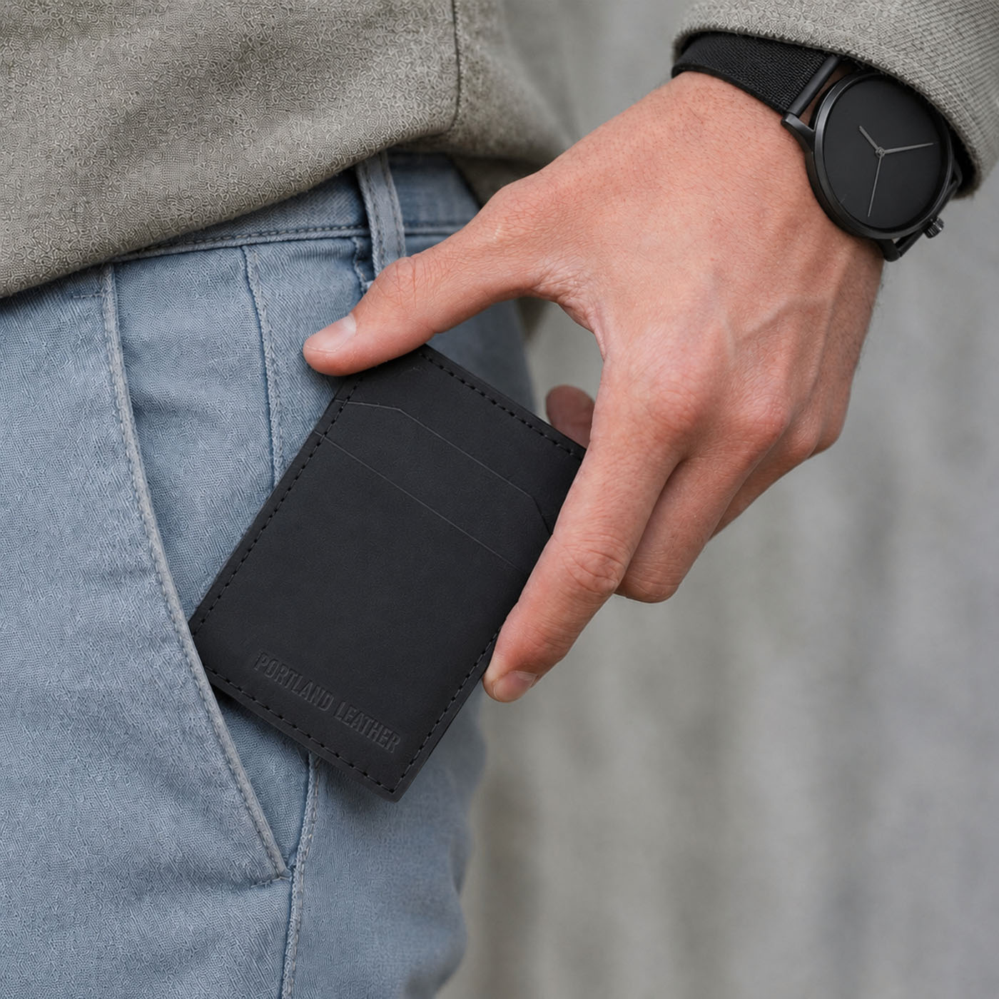 Nero | A model putting a black leather card holder into jeans.