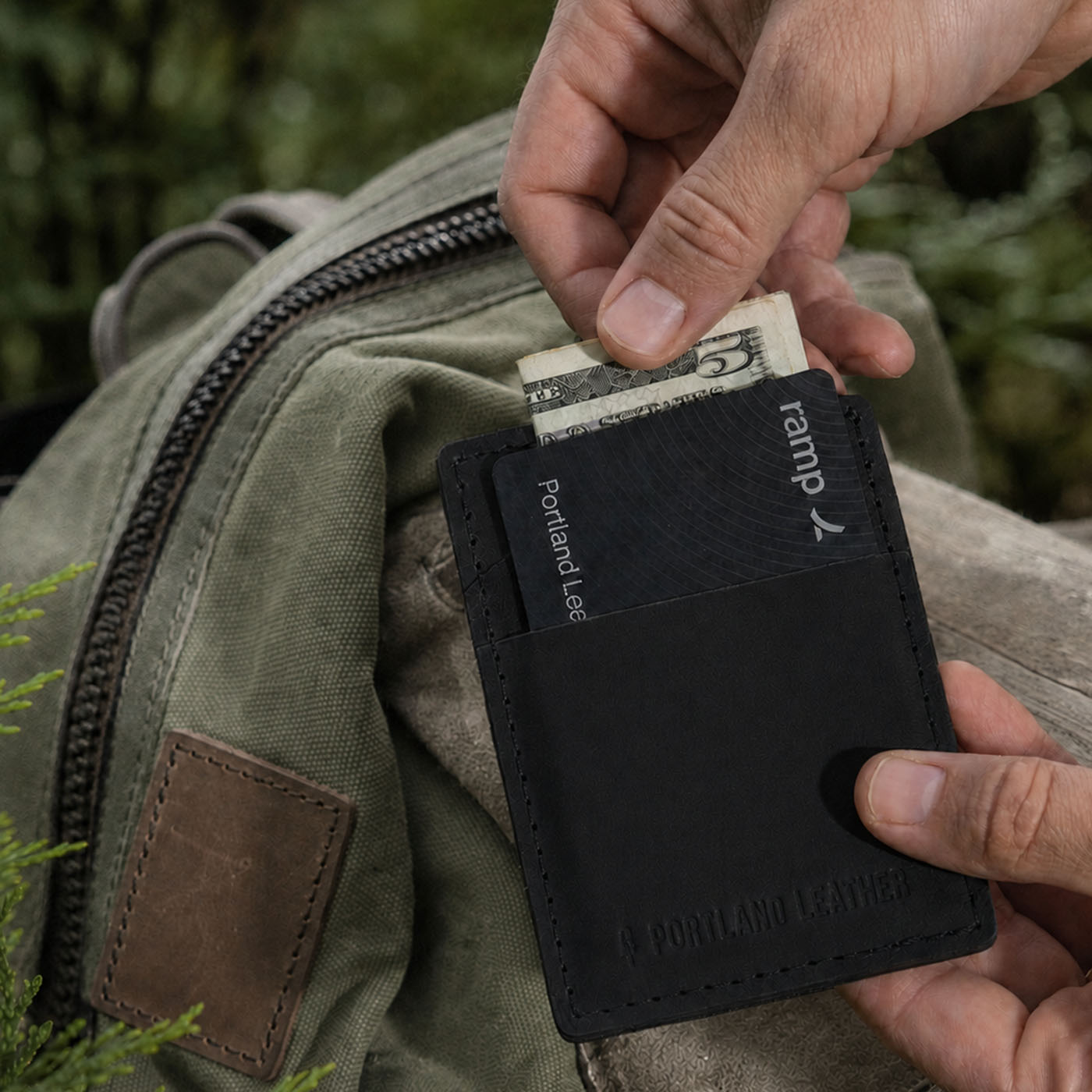 Nero | A close-up of a black leather card holder wallet being held in front of backpack.