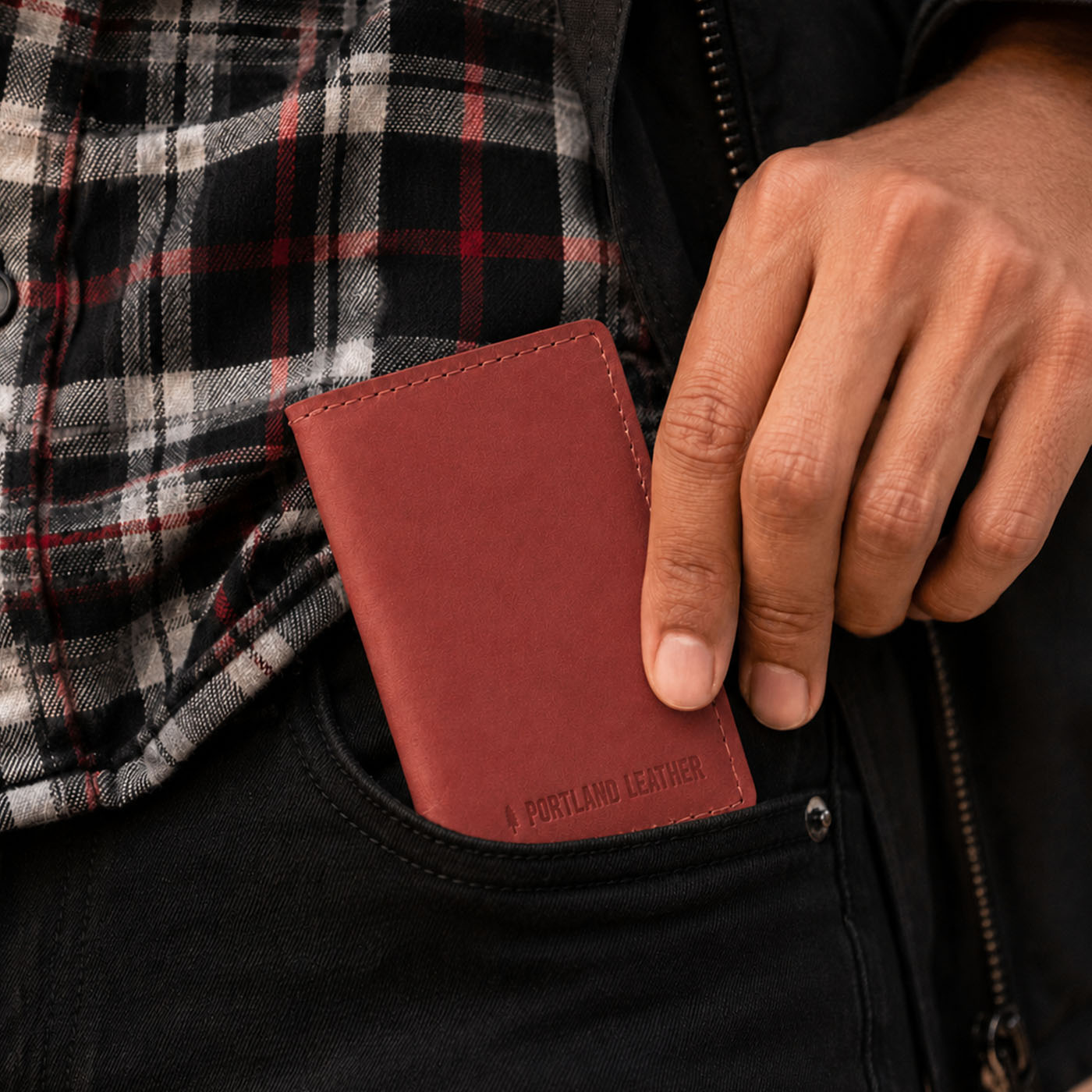 Marrone | A close up of a model sliding a leather card holder into their pants pocket