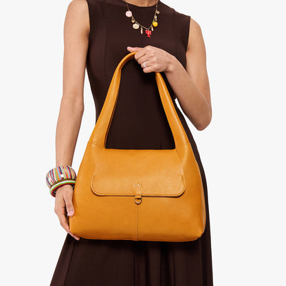 Sunshine*Medium | A model holding a slouchy triangle shaped shoulder bag with a flap