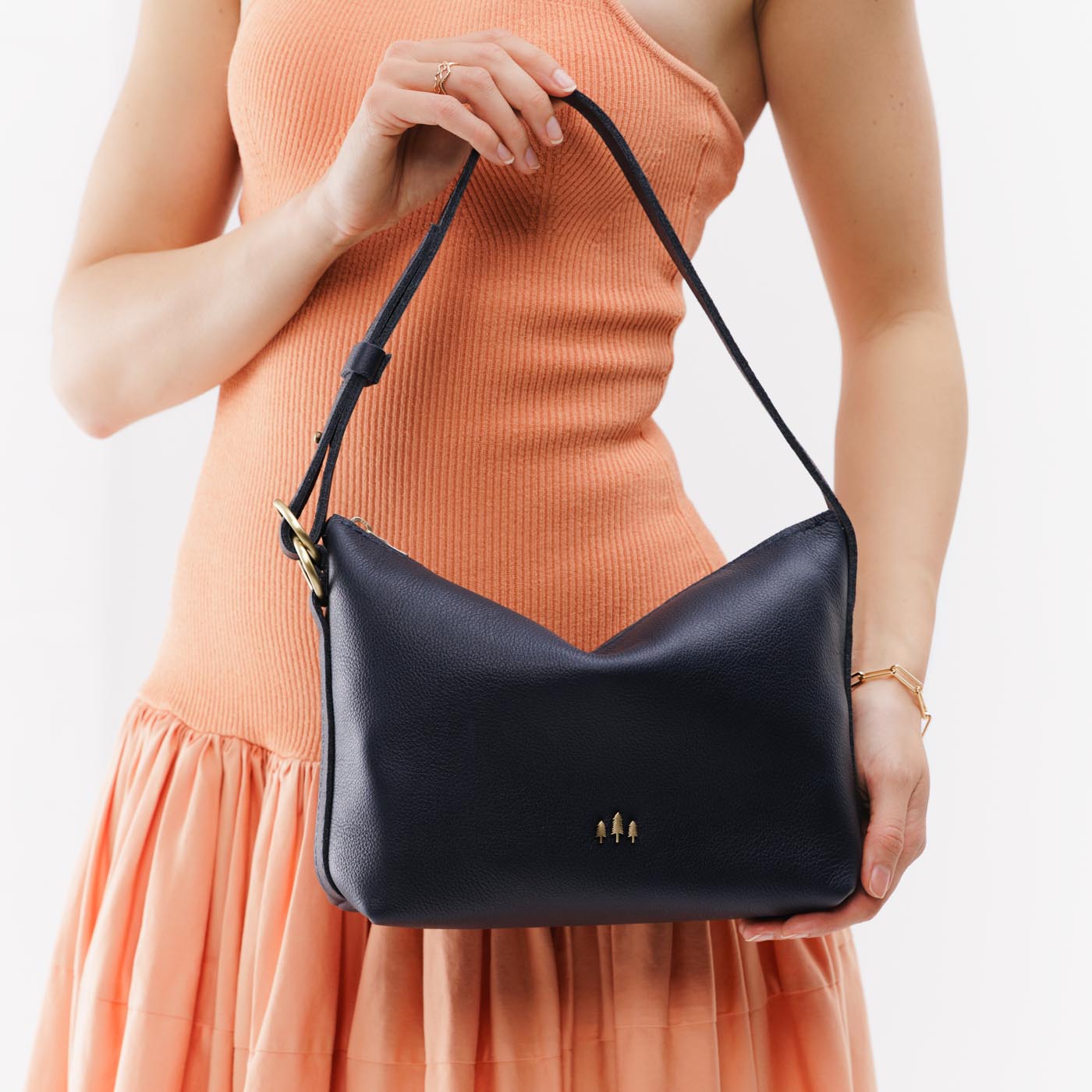 Night Owl*Small | Model holding petite slouchy leather shoulder bag with zipper opening and three metal tree emblems