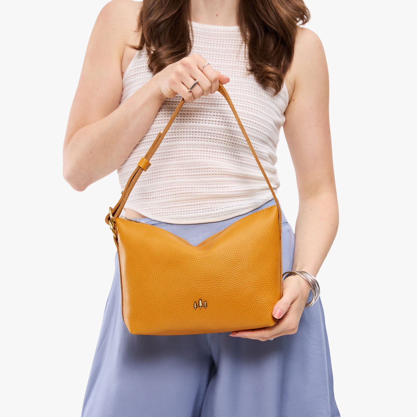 Sunshine*Small | Model holding a Slouchy Shoulder Bag that has a zipper opening and three metal tree emblems