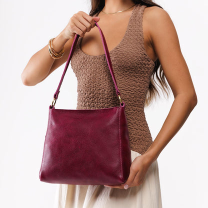 Orchid*Small | Model carrying leather triangular shoulder bag with zipper top closure and wide shoulder strap